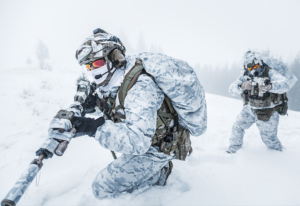Military soldiers in winter camo, carrying weapons in deep snow.